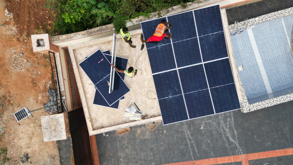 Aerial view of technicians installing solar panels on the rooftop of a building, with multiple solar panels arranged across the roof.